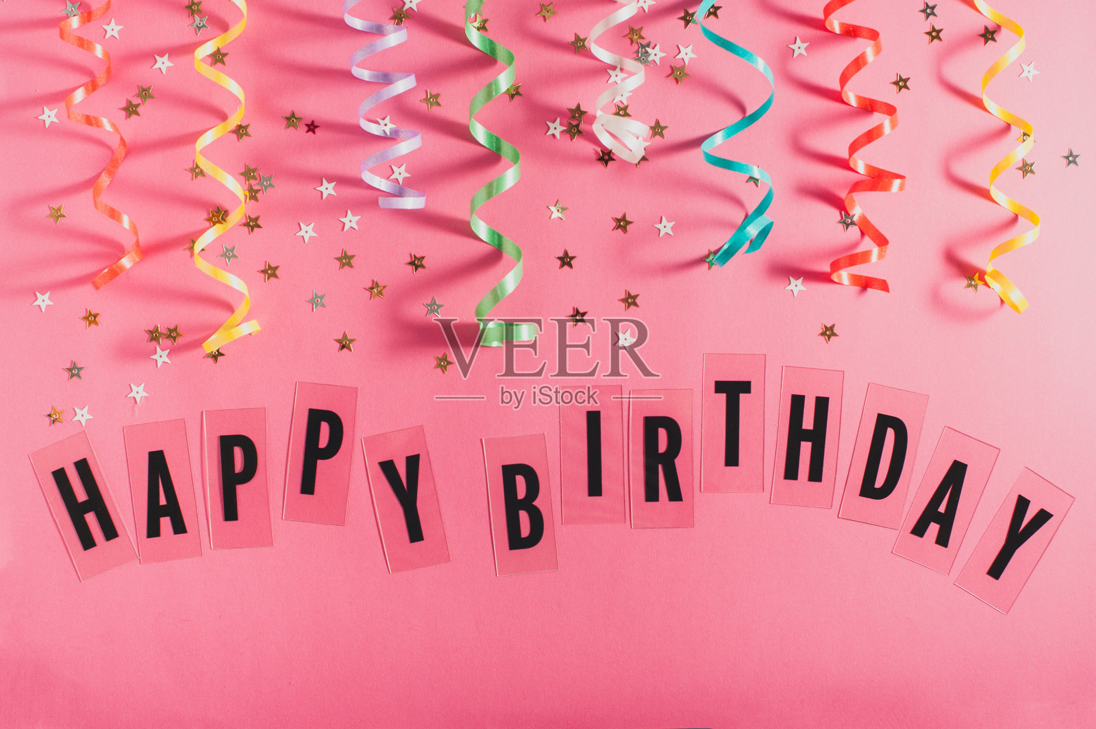 五颜六色的派对彩带，金色的小星星，粉红色背景上写着生日快乐。女孩生日的概念。平的。照片摄影图片