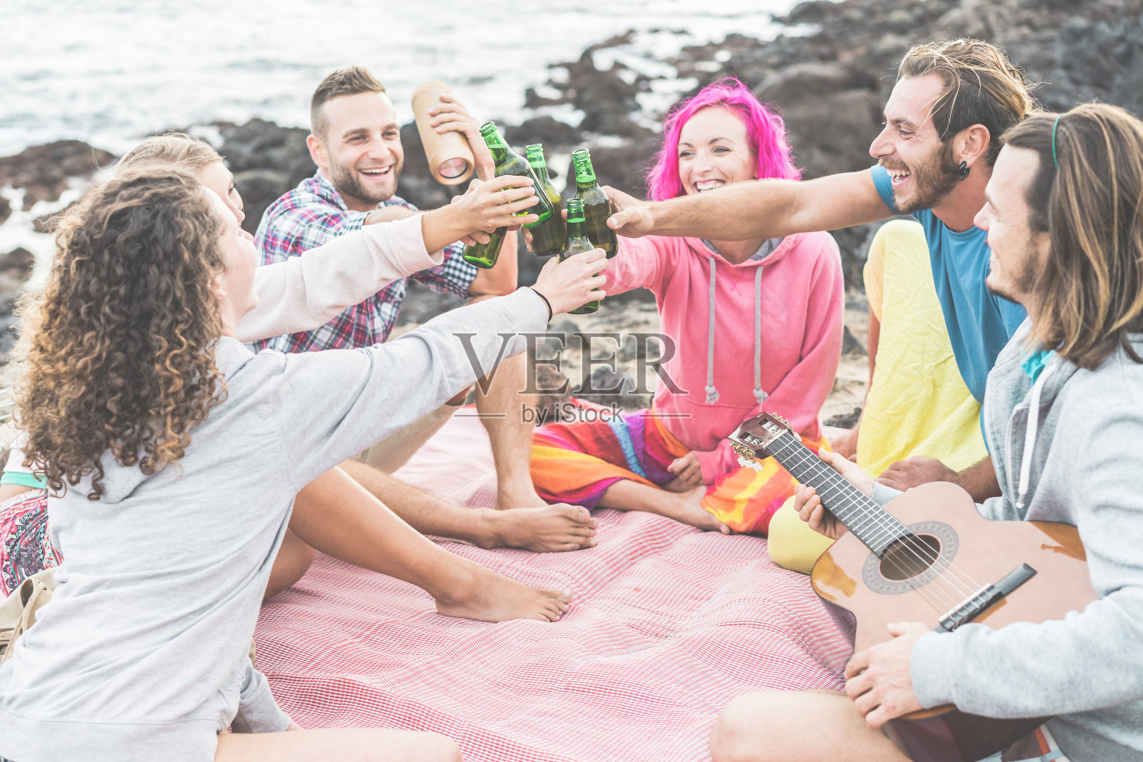 快乐的朋友欢呼与啤酒和演奏音乐在户外露营-时髦的人有乐趣一起做野餐-友谊，青年生活方式和度假概念-专注于手瓶照片摄影图片