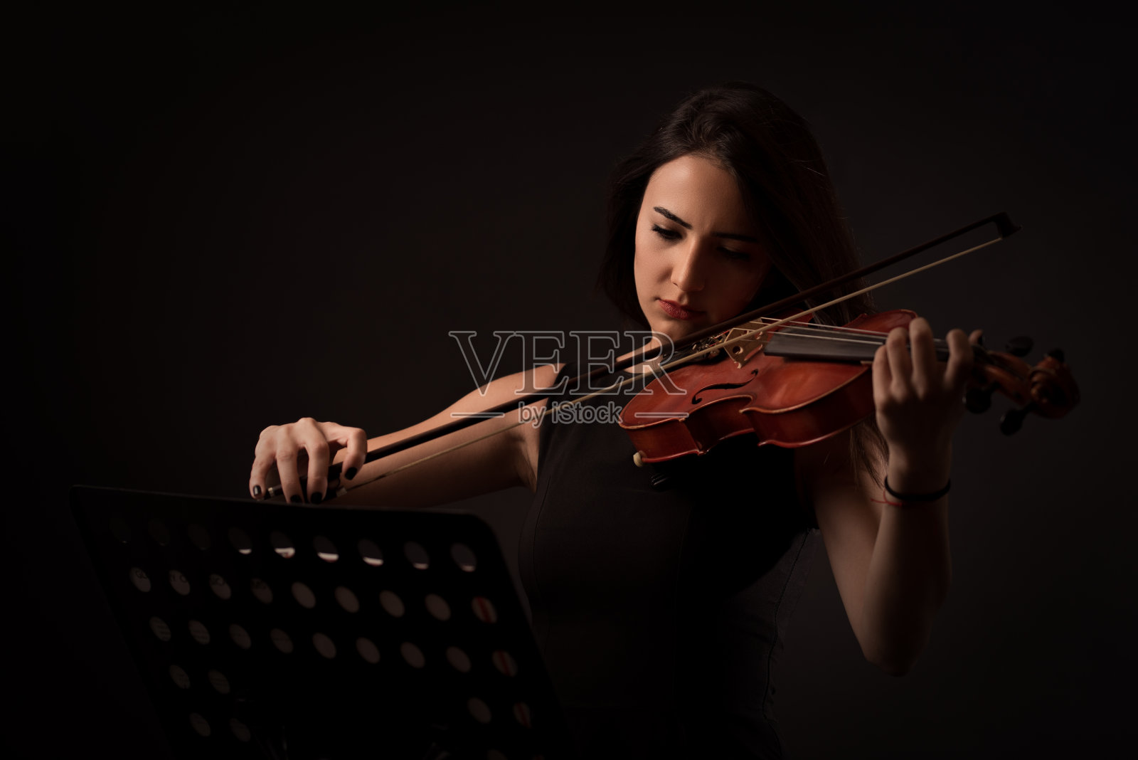 美丽的年轻女子在黑色的背景上拉着小提琴照片摄影图片