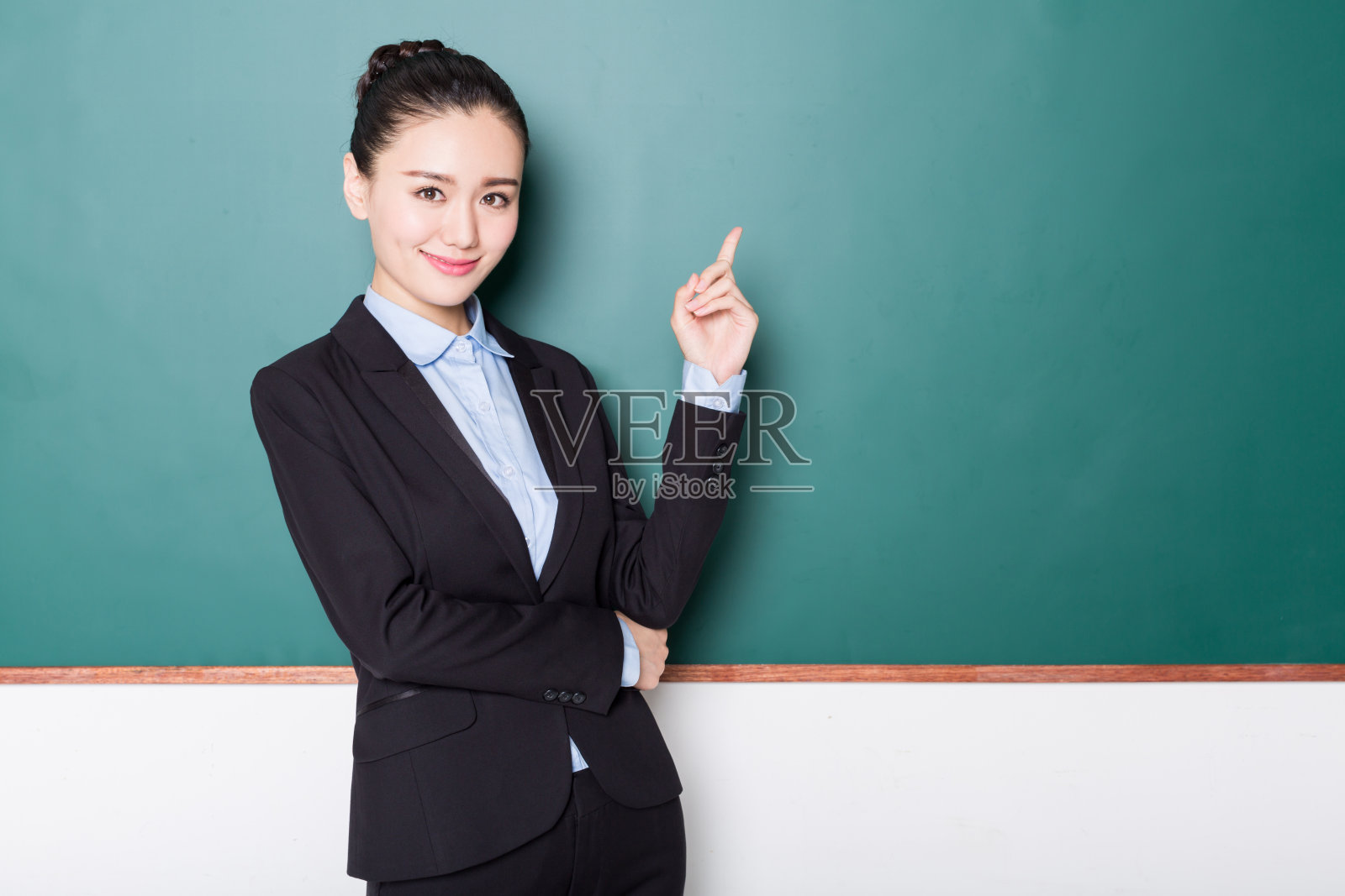 年轻女教师指着黑板，画像。照片摄影图片