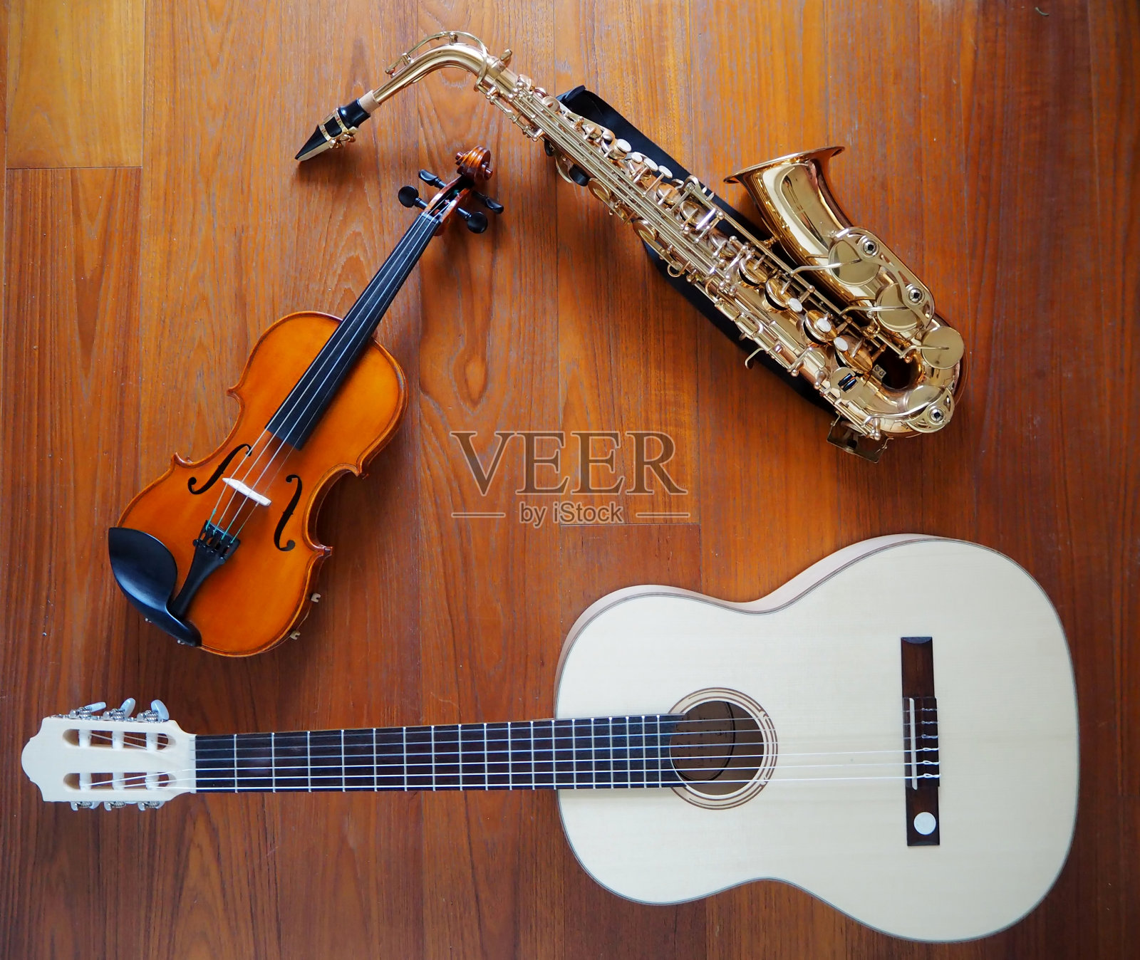 一把小提琴，一把吉他和一把萨克斯管靠在一起。柚木木材背景。照片摄影图片