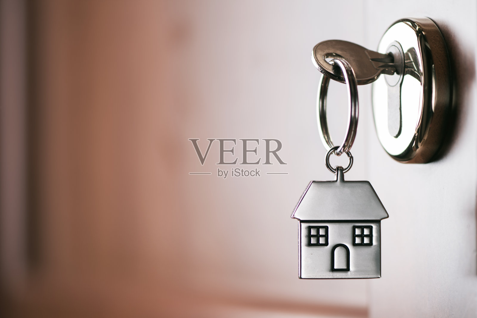 房子钥匙挂在一个房子形状的银钥匙圈上，锁在一扇棕色大门的锁上照片摄影图片