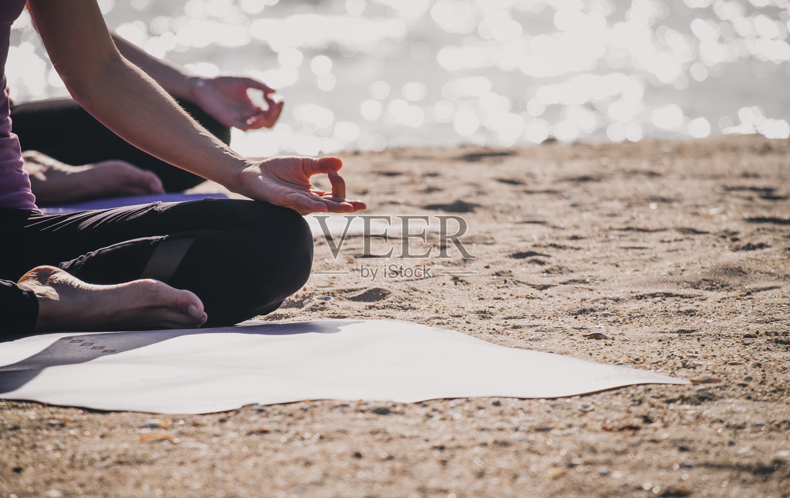 靠近的手瑜伽大师坐做手相和冥想在海滩在海岸线，平静和放松的概念，健康和健康的生活方式。照片摄影图片