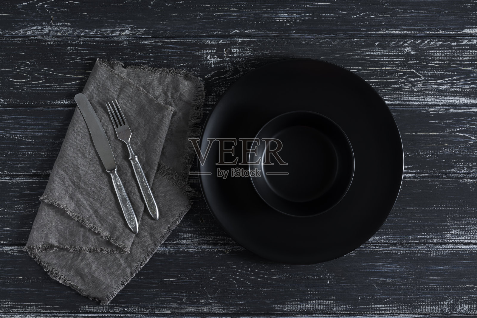 空空的黑色盘子，餐巾上的刀叉，质朴的黑色背景。从上面看，水平投影。照片摄影图片