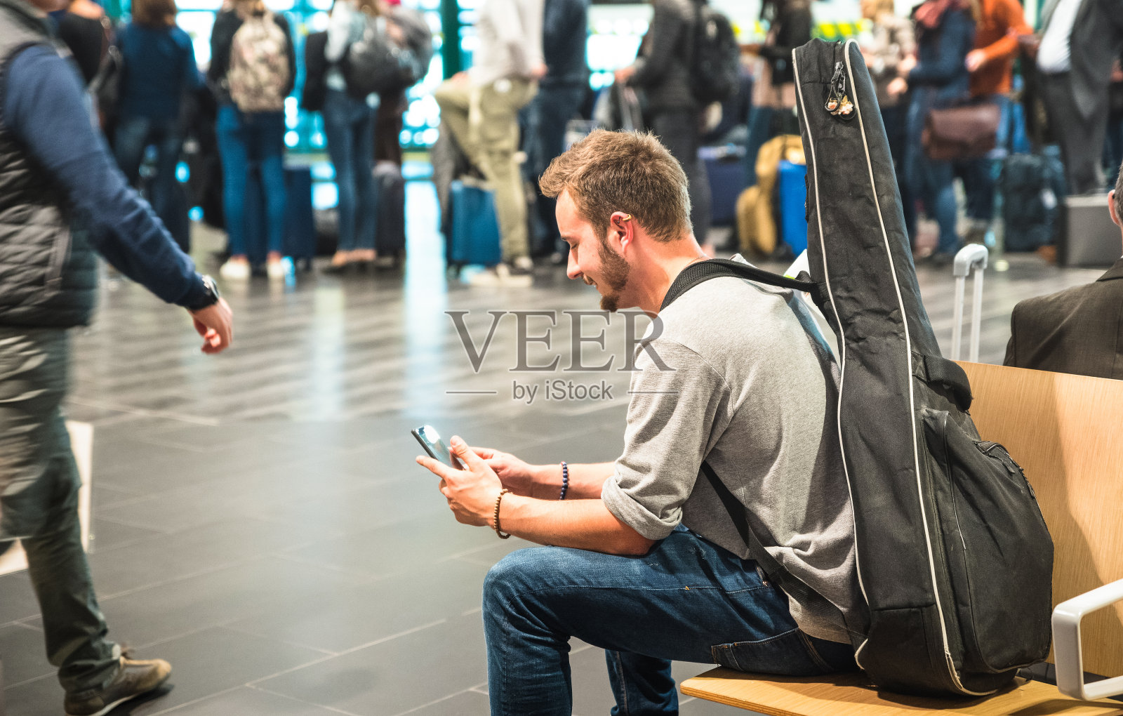 在国际机场使用手机的潮人-在候机楼门口等待飞机的人-带着吉他背包的旅行概念-专注于脸照片摄影图片