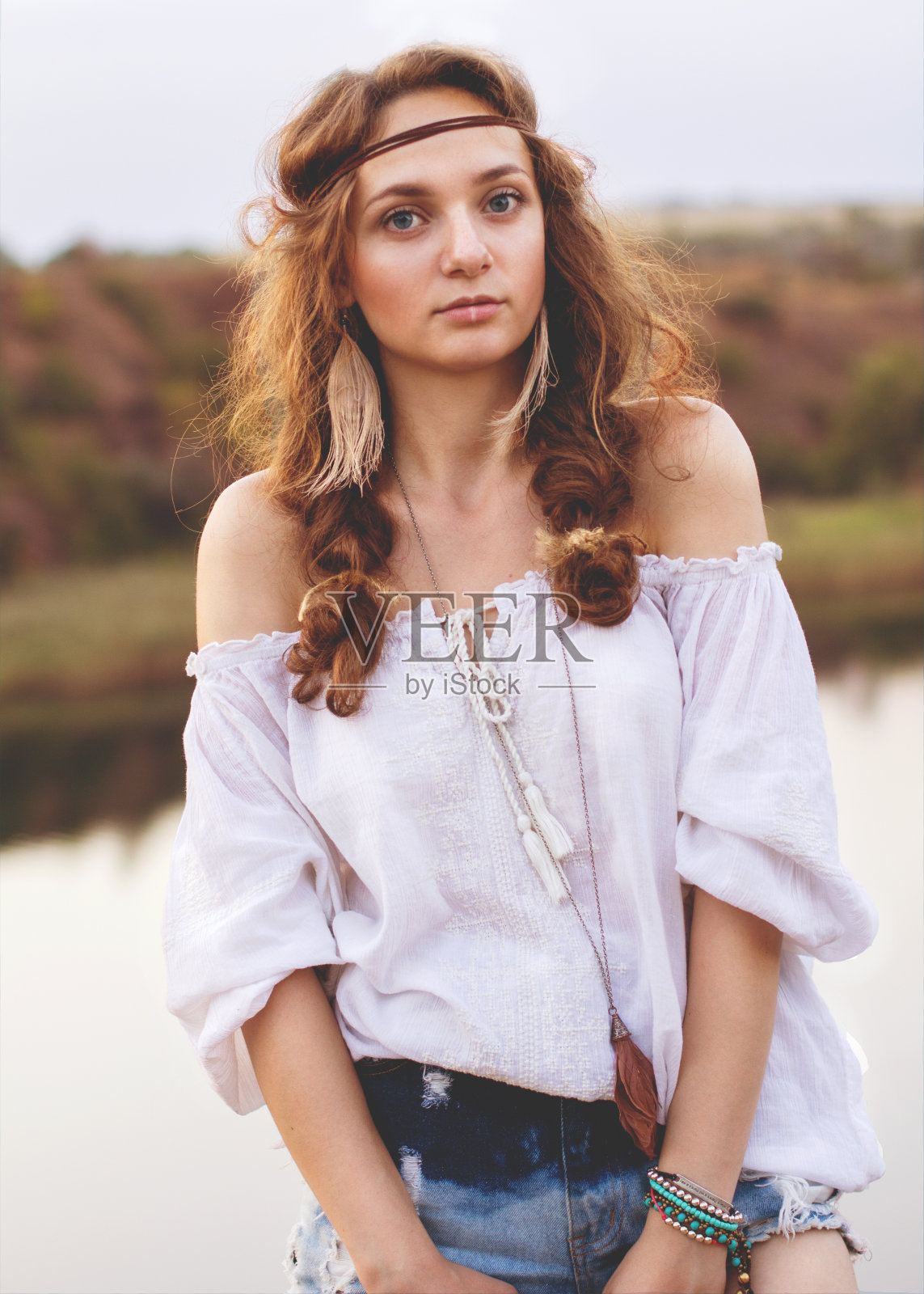 一个可爱的波西米亚风格的女孩的肖像在一个湖的背景。柔和温暖的复古照片颜色。照片摄影图片