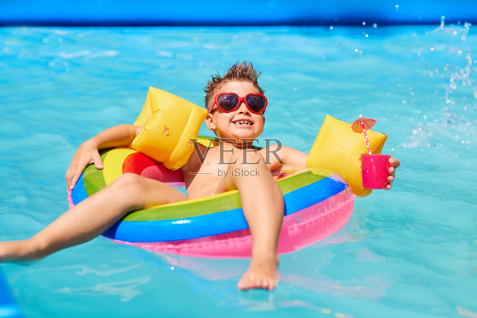 戴着墨镜的快乐小孩在泳池里喝着鸡尾酒。照片摄影图片