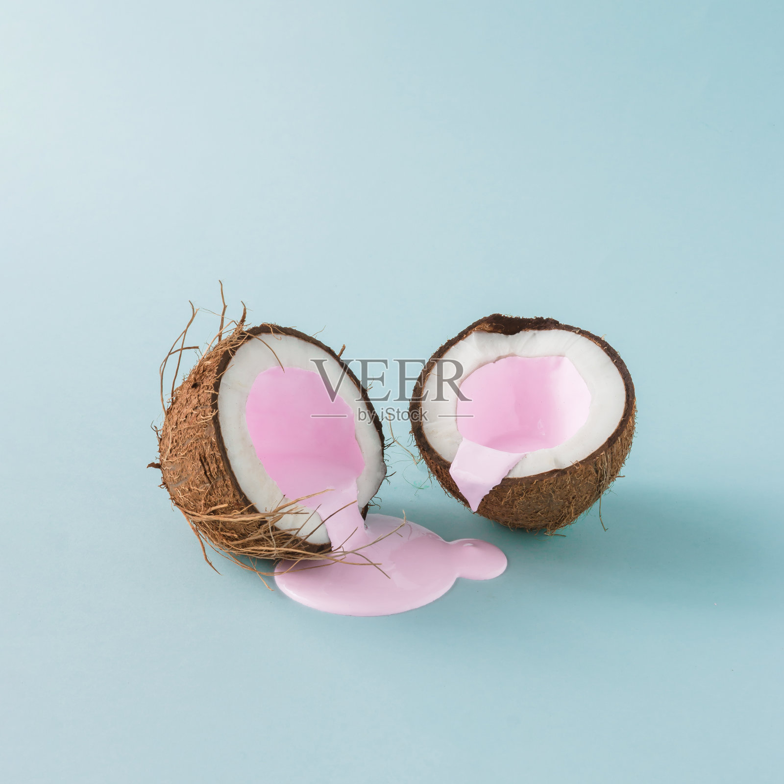 把椰子撕成两半，倒入粉色牛奶。极简主义。食品创意概念。照片摄影图片