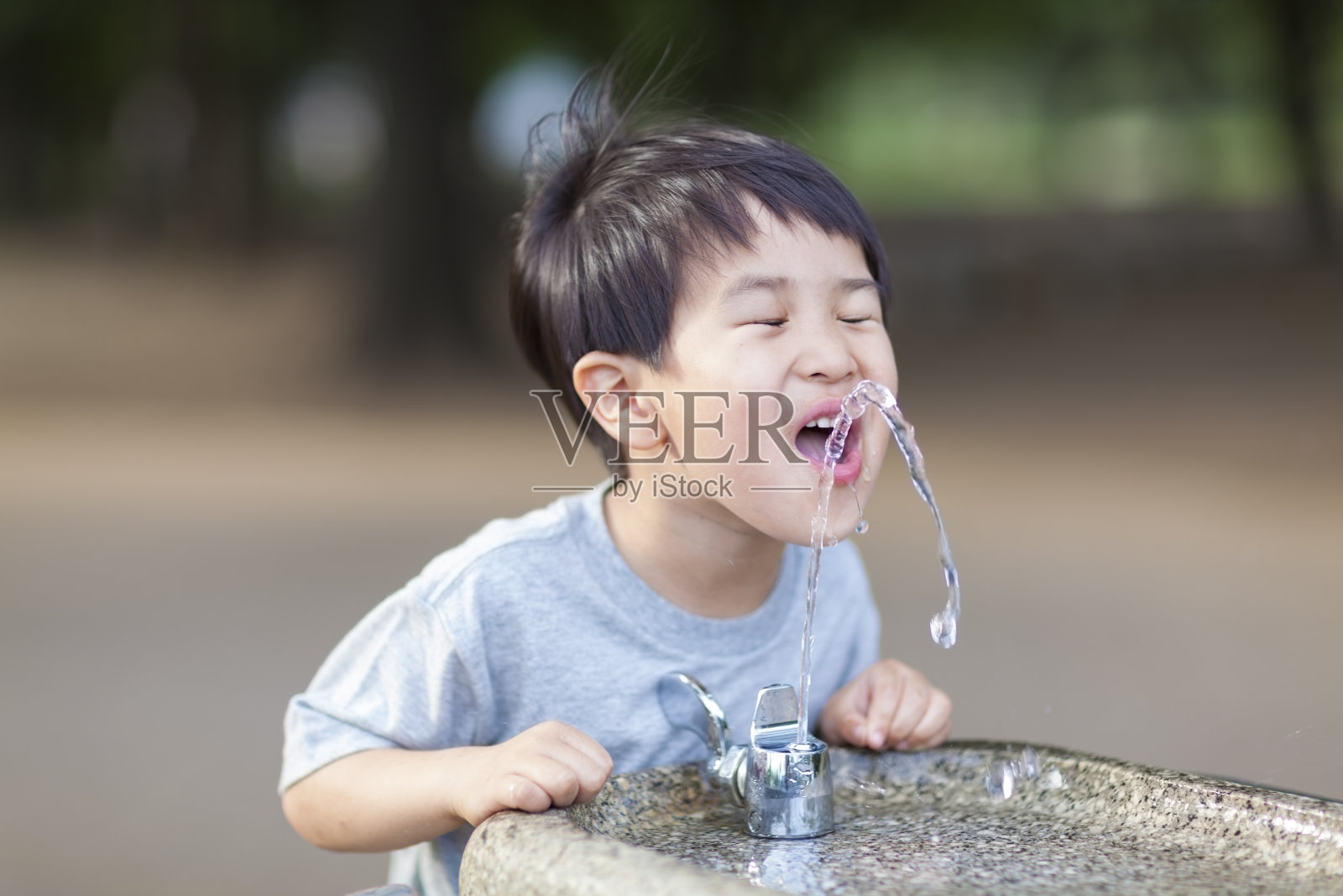 从饮水机里喝水的男孩照片摄影图片