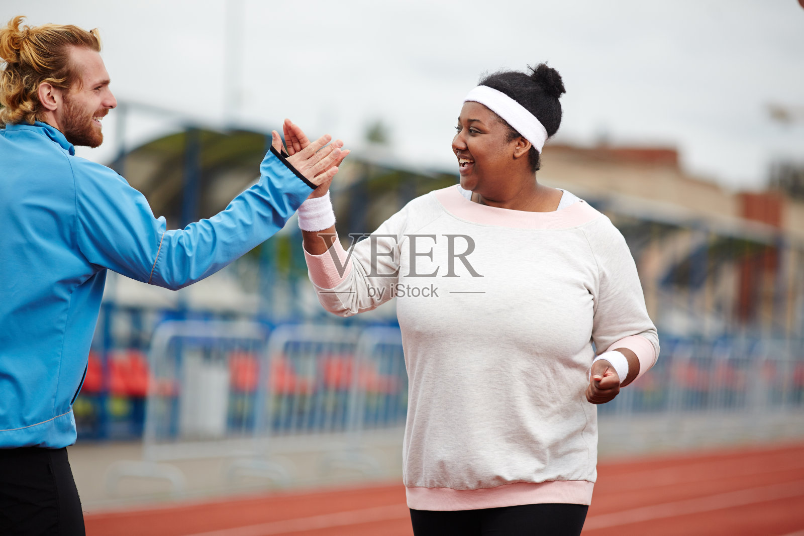 快乐的胖女人在赛道上跑步时与她的私人教练击掌照片摄影图片