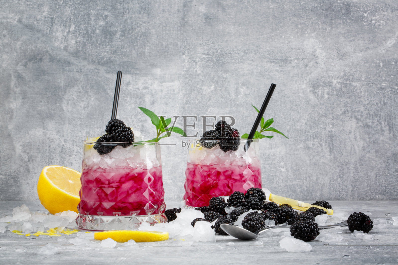 两杯冰鸡尾酒。冷贝瑞饮料。饮料与薄荷，柠檬柠檬和黑莓在冰冻的白色背景。照片摄影图片