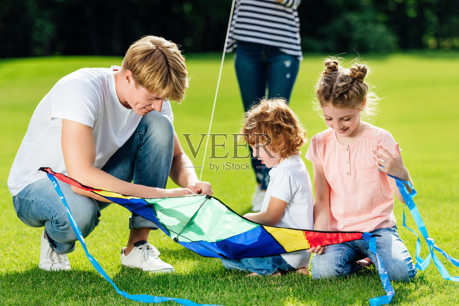 快乐的父亲和两个孩子在公园的草地上玩风筝照片摄影图片
