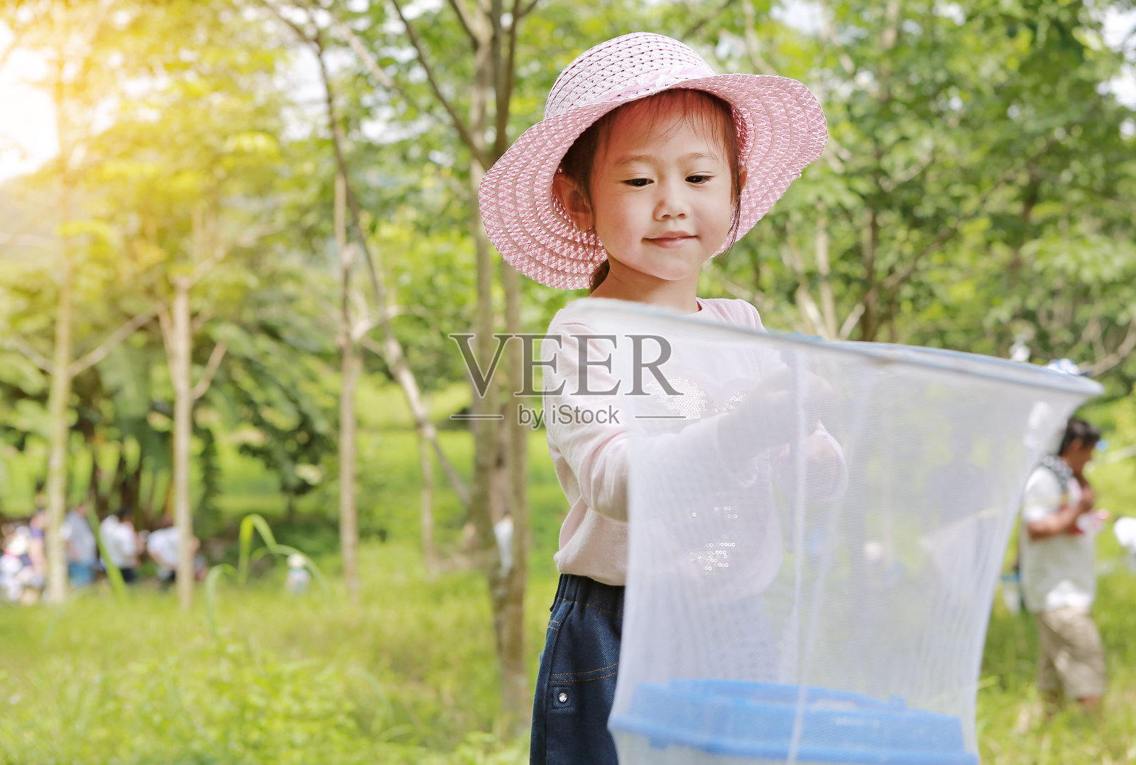 可爱的亚洲女孩戴着草帽和蚊帐在田野里玩夏天。照片摄影图片