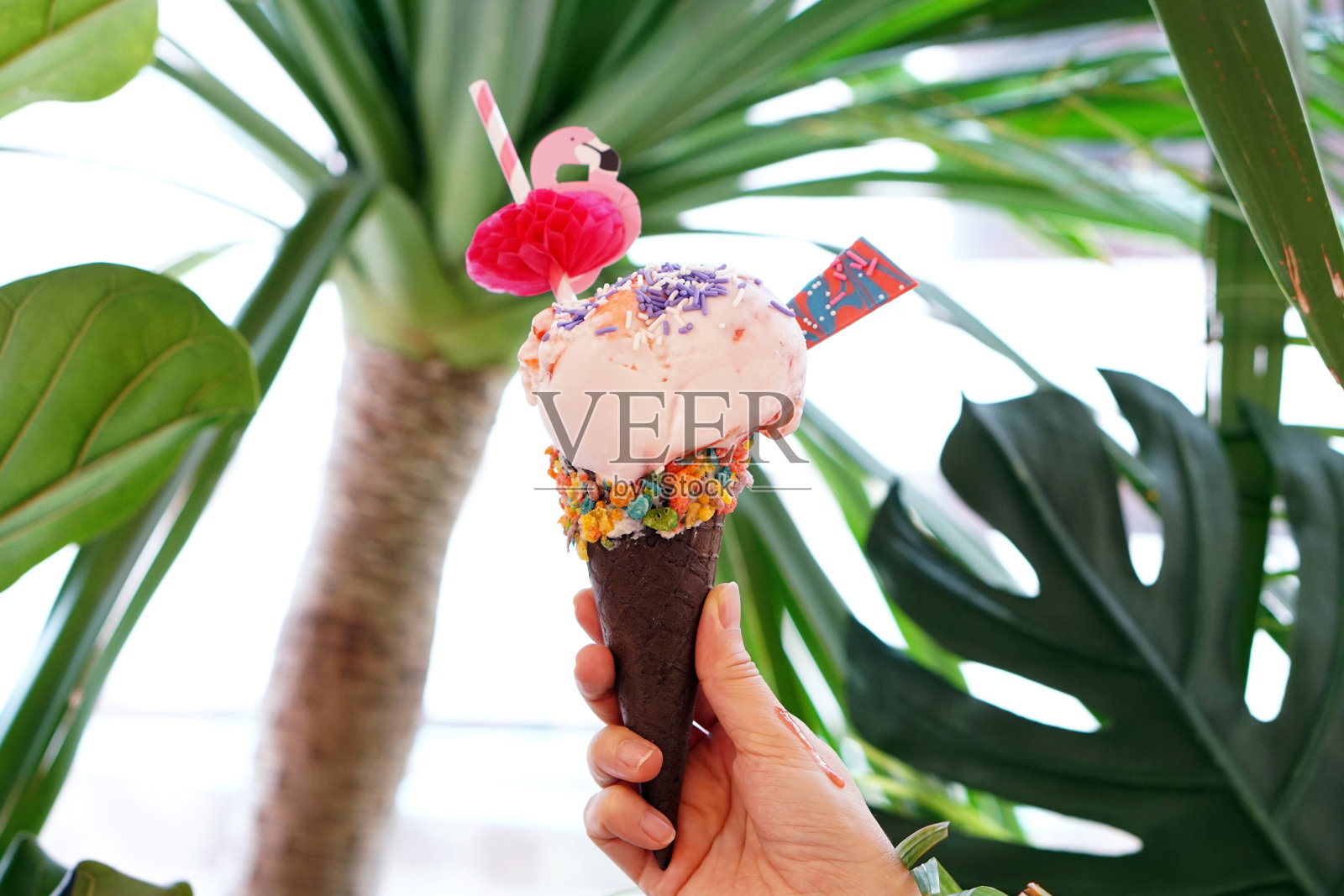 手握梦幻冰淇淋筒，模糊的背景上点缀着彩虹点缀的草莓酸奶，尽情享用吧。照片摄影图片
