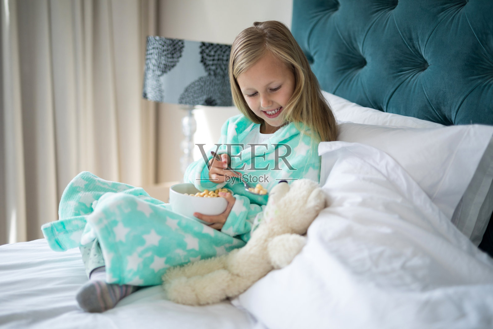 微笑的女孩给床上的小熊喂早餐照片摄影图片