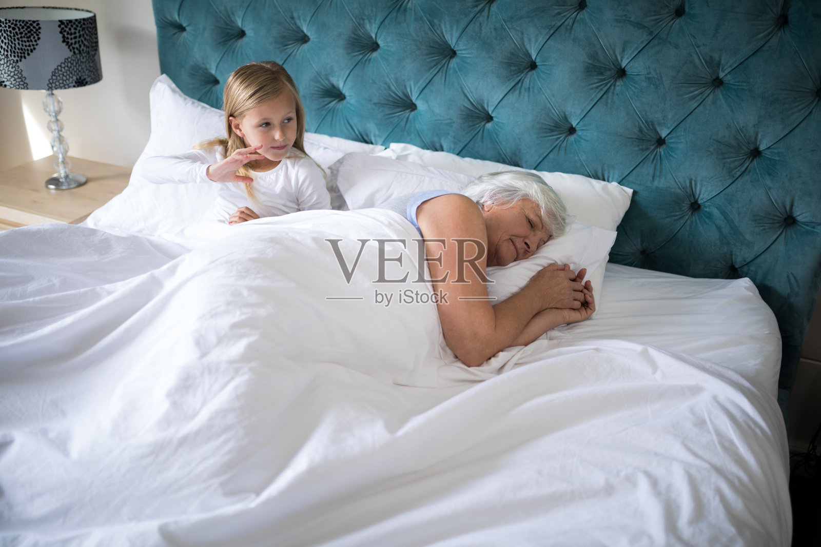 奶奶睡在床上，女孩坐在她后面照片摄影图片