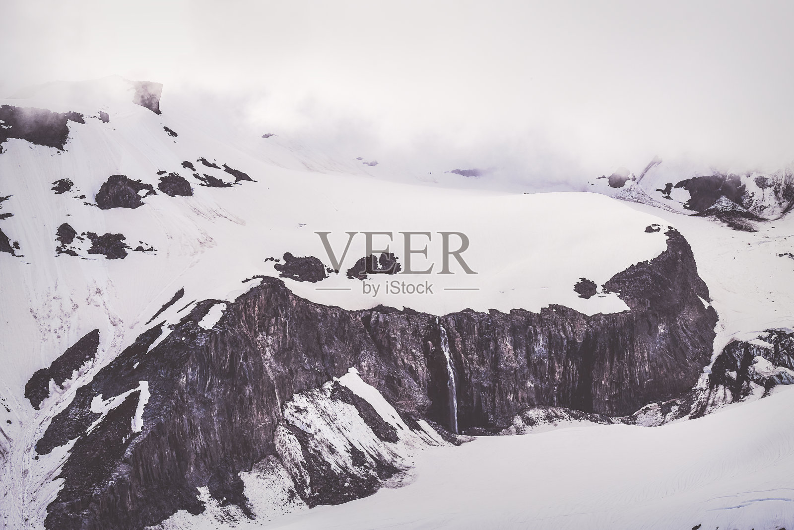 白雪覆盖的山脊和小溪流从悬崖上倾泻而下照片摄影图片