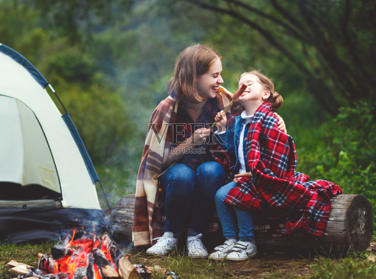 快乐旅游家庭旅行徒步。妈妈和孩子在帐篷附近的篝火上煎香肠照片摄影图片