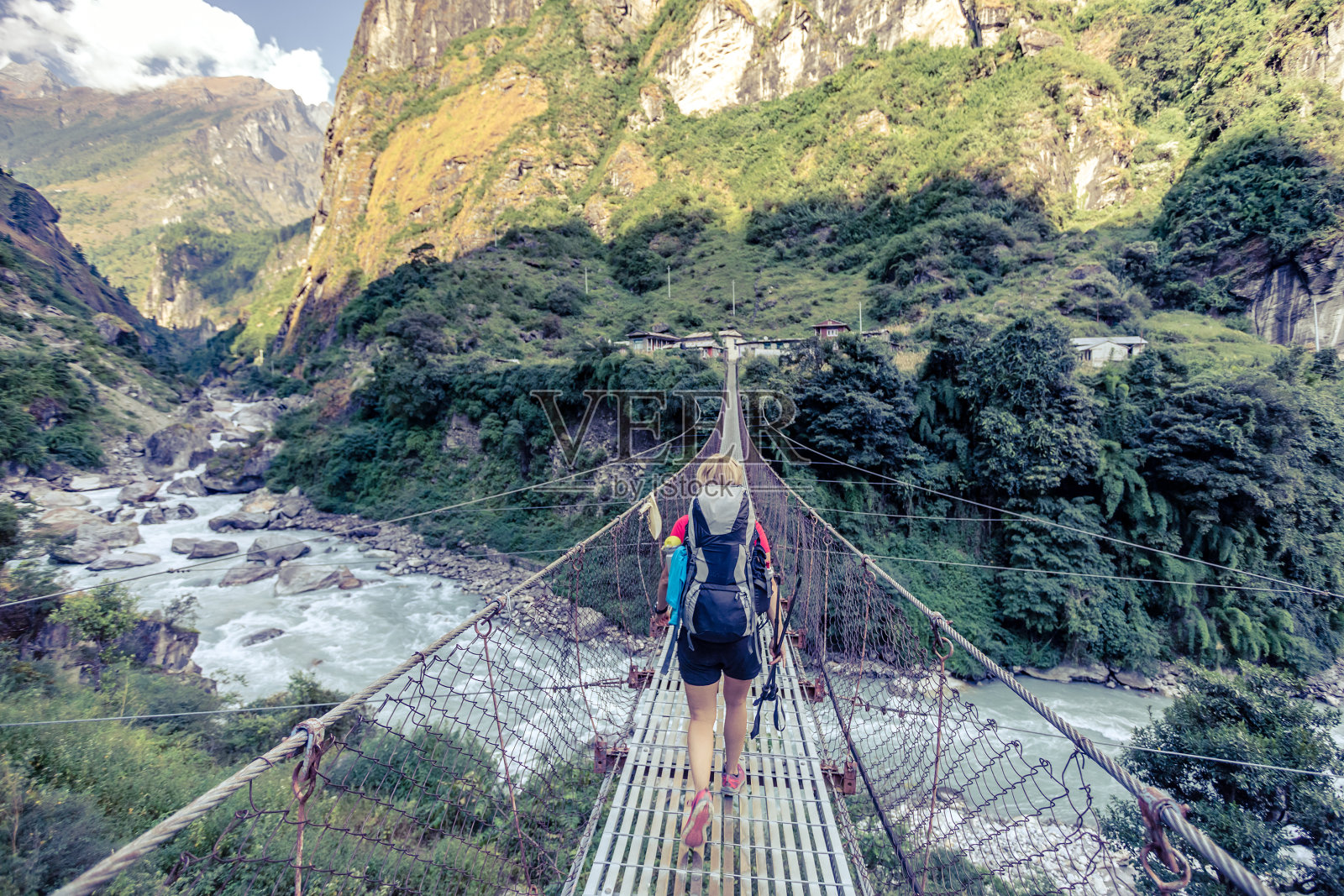 一名女子背包客穿过尼泊尔喜马拉雅山的吊桥照片摄影图片