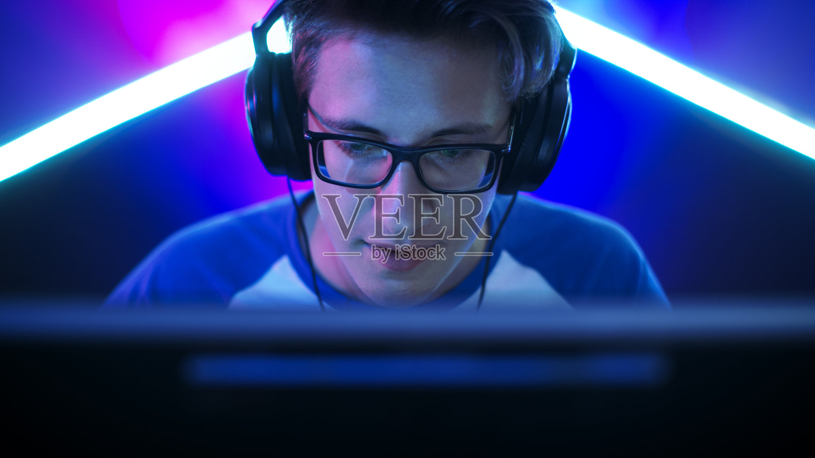 职业玩家在他的电脑上玩MMORPG/策略/射击电子游戏。他参加网络游戏比赛，在家里玩，或在网吧玩。他戴着眼镜和游戏耳机，对着麦克风讲话。照片摄影图片
