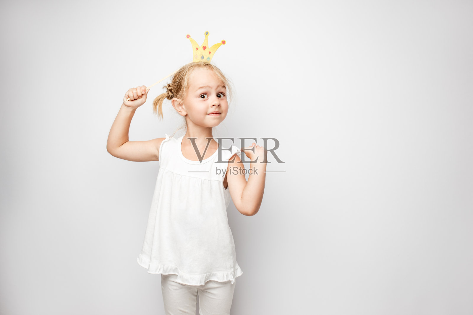 美丽的小女孩与纸冠摆姿势在白色的背景在家里。照片摄影图片