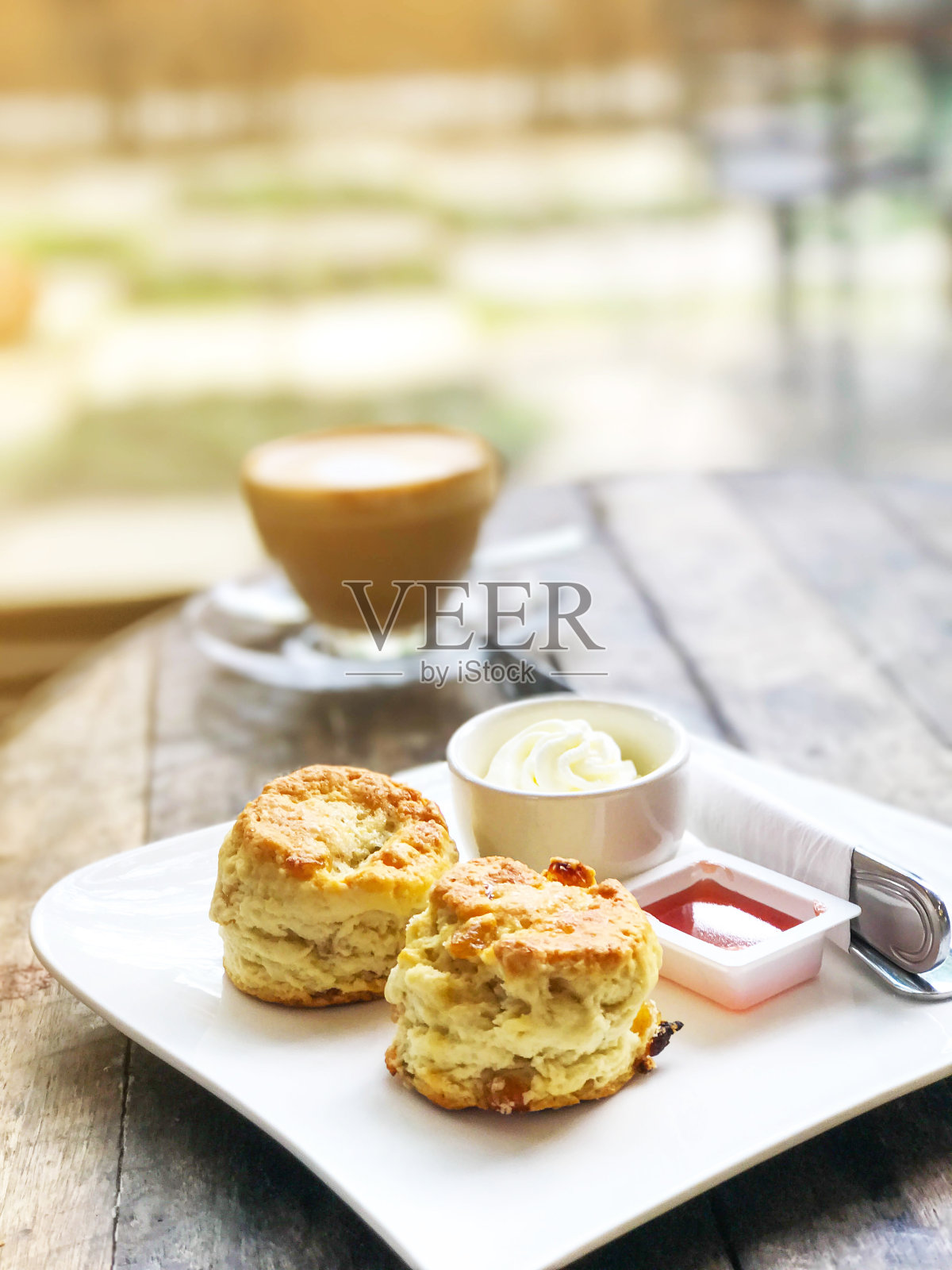 木桌上的白色盘子里放着烤饼、抹奶油和果酱，背景是一杯咖啡照片摄影图片