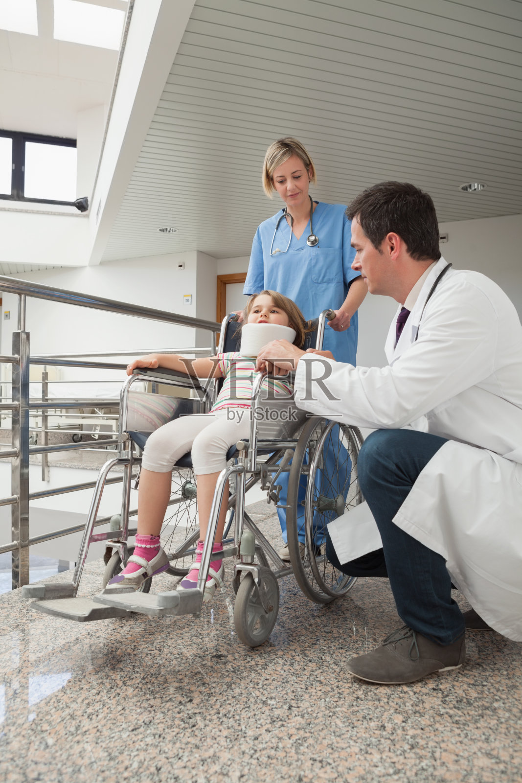 医生蹲在轮椅上的孩子旁边，护士推着轮椅照片摄影图片
