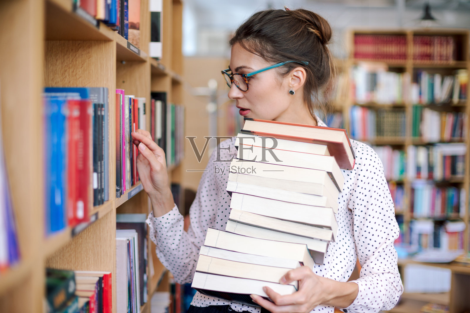 在图书馆里有一堆书的年轻女子想要更多照片摄影图片