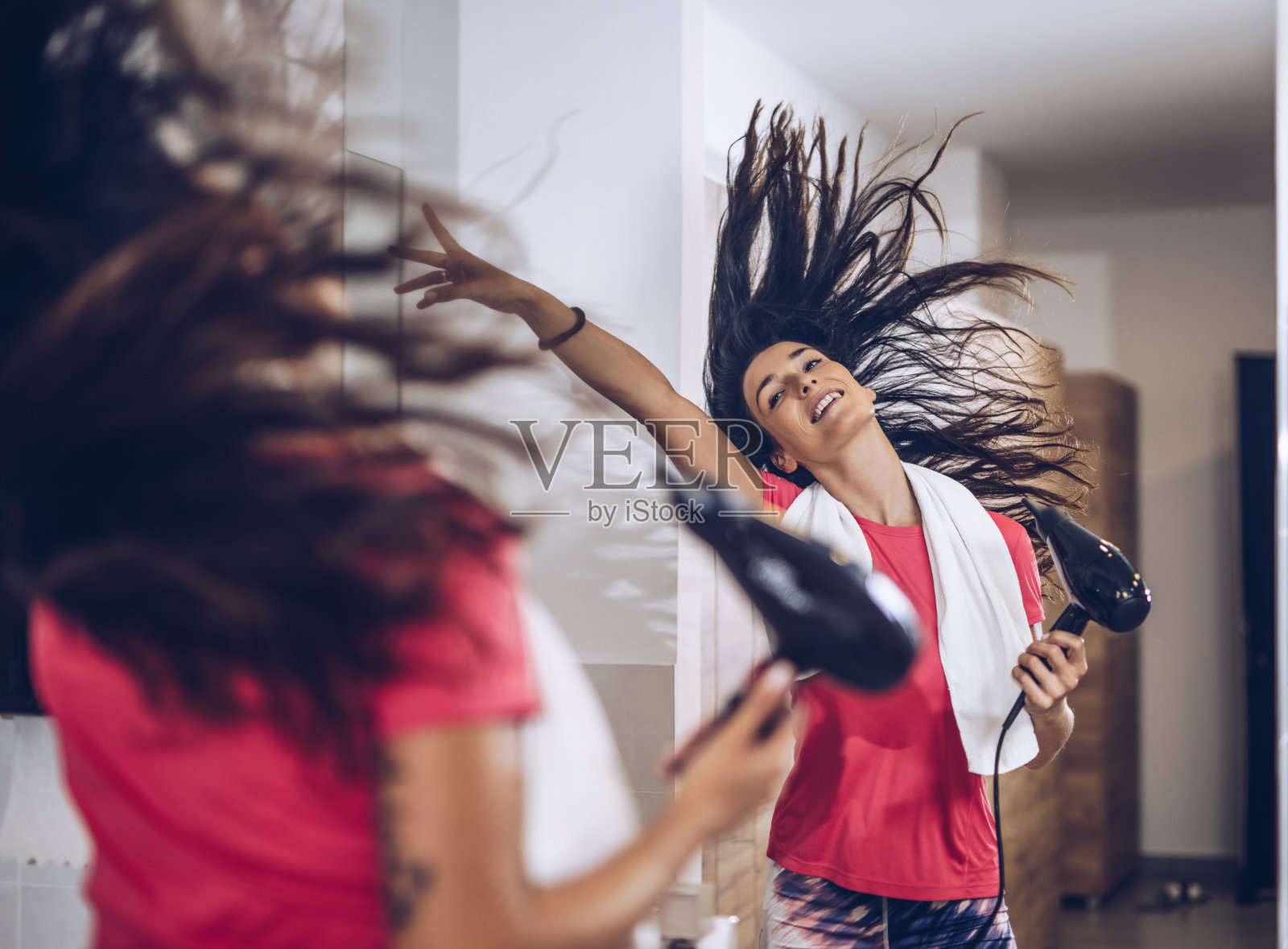 镜子里的映像，一个女人正在玩，在更衣室里吹干她的头发。照片摄影图片