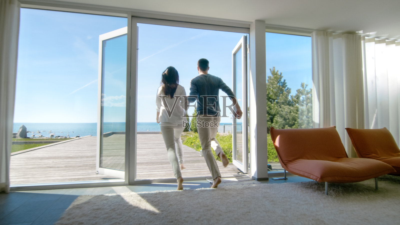 幸福的年轻夫妇牵着手跑出他们的家到阳台与海边的景色。照片摄影图片