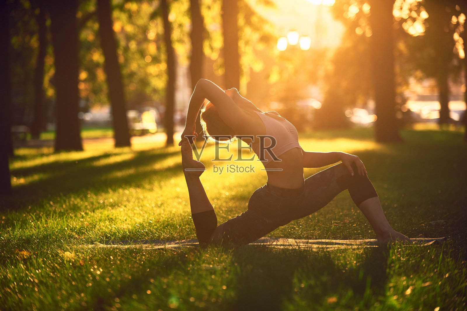 美丽的年轻女子练习瑜伽体式国王鸽子姿势rajakapotasana在公园日落照片摄影图片