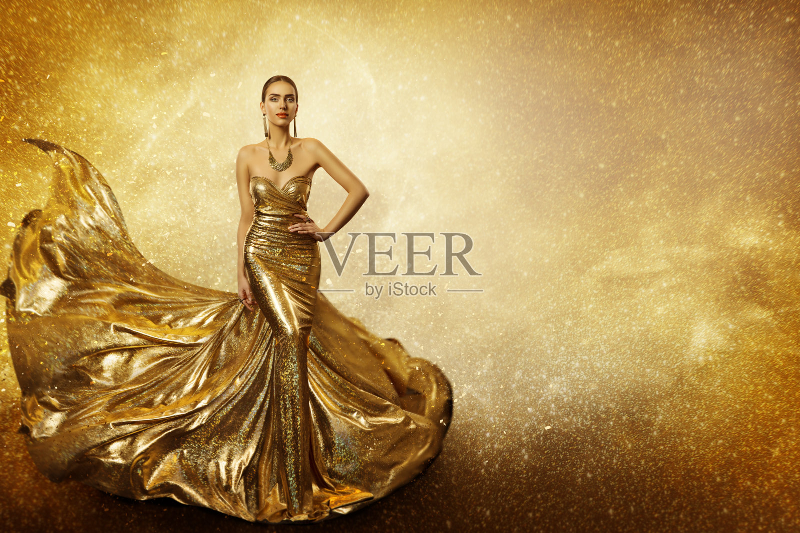 金色的时尚模特，优雅的女人飞翔的金色连衣裙，挥舞着闪闪发光的长袍面料照片摄影图片
