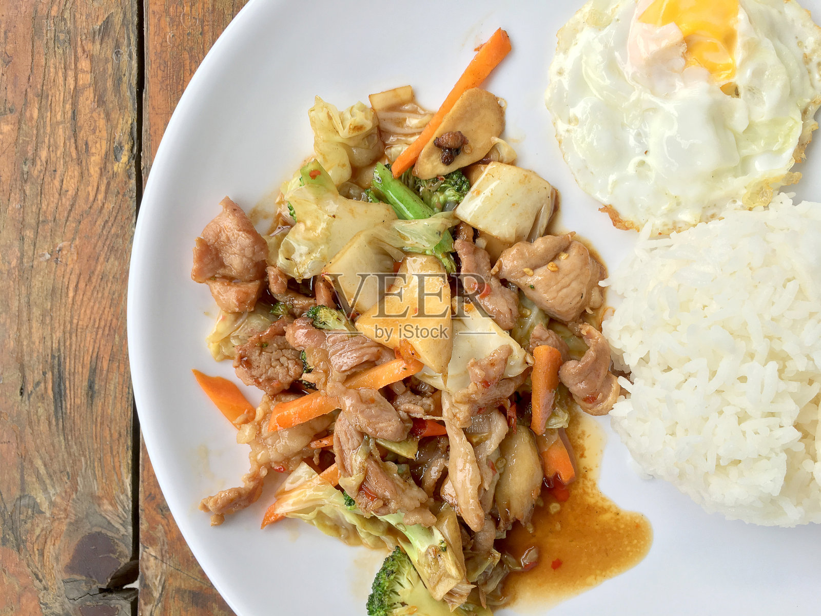 泰式辣味食物:在木桌上的白盘里放一盘猪肉炒蔬菜和炒蛋饭。健康的菜肴。照片摄影图片