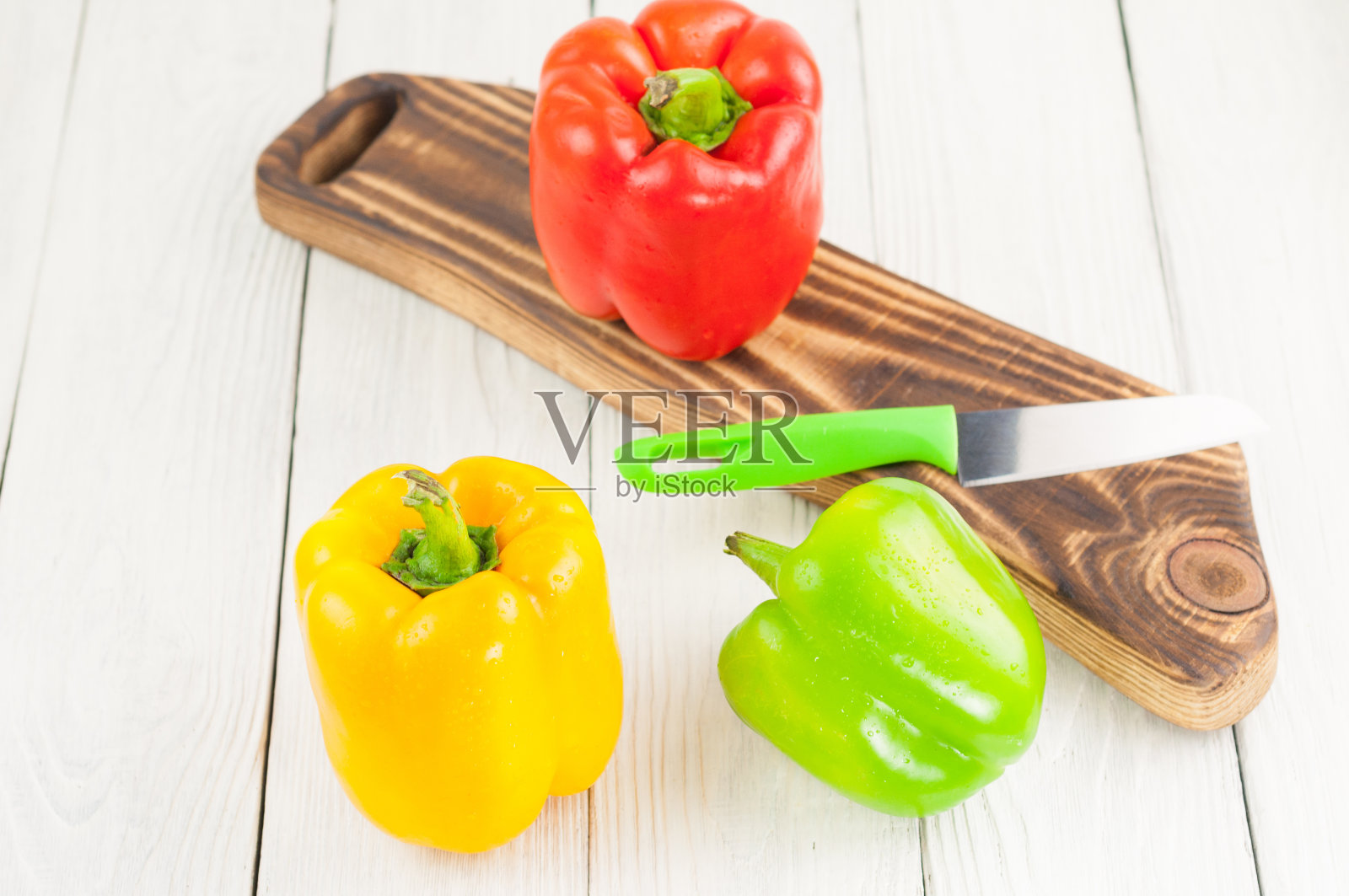 一排红、黄、绿的新鲜辣椒，放在乡村菜板上，旁边是一把锋利的刀，放在古老的乡村木板上照片摄影图片