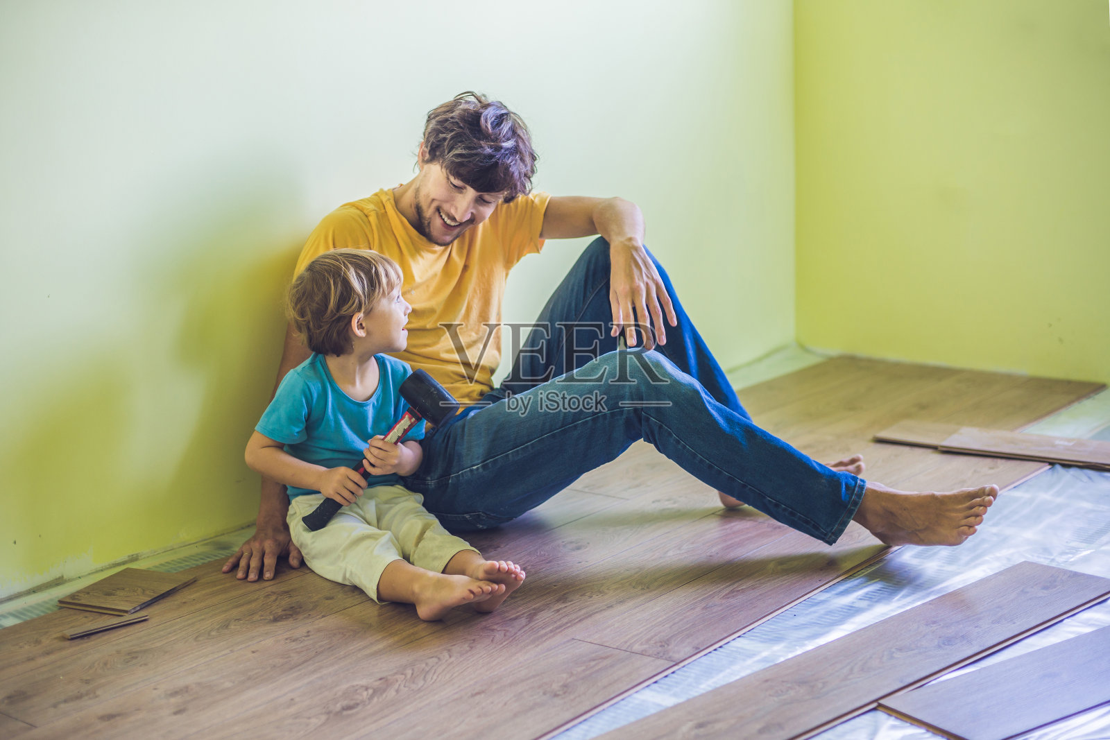父亲和儿子安装新的木质强化地板。强化地板下红外线地板采暖系统照片摄影图片