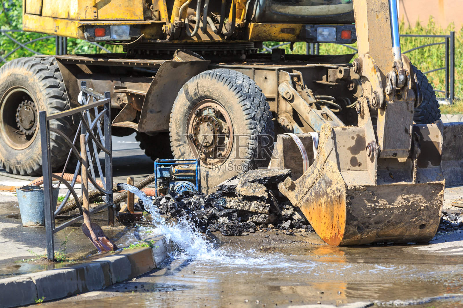 挖掘机有助于消除炎热的夏天在街上弄断水管的问题照片摄影图片