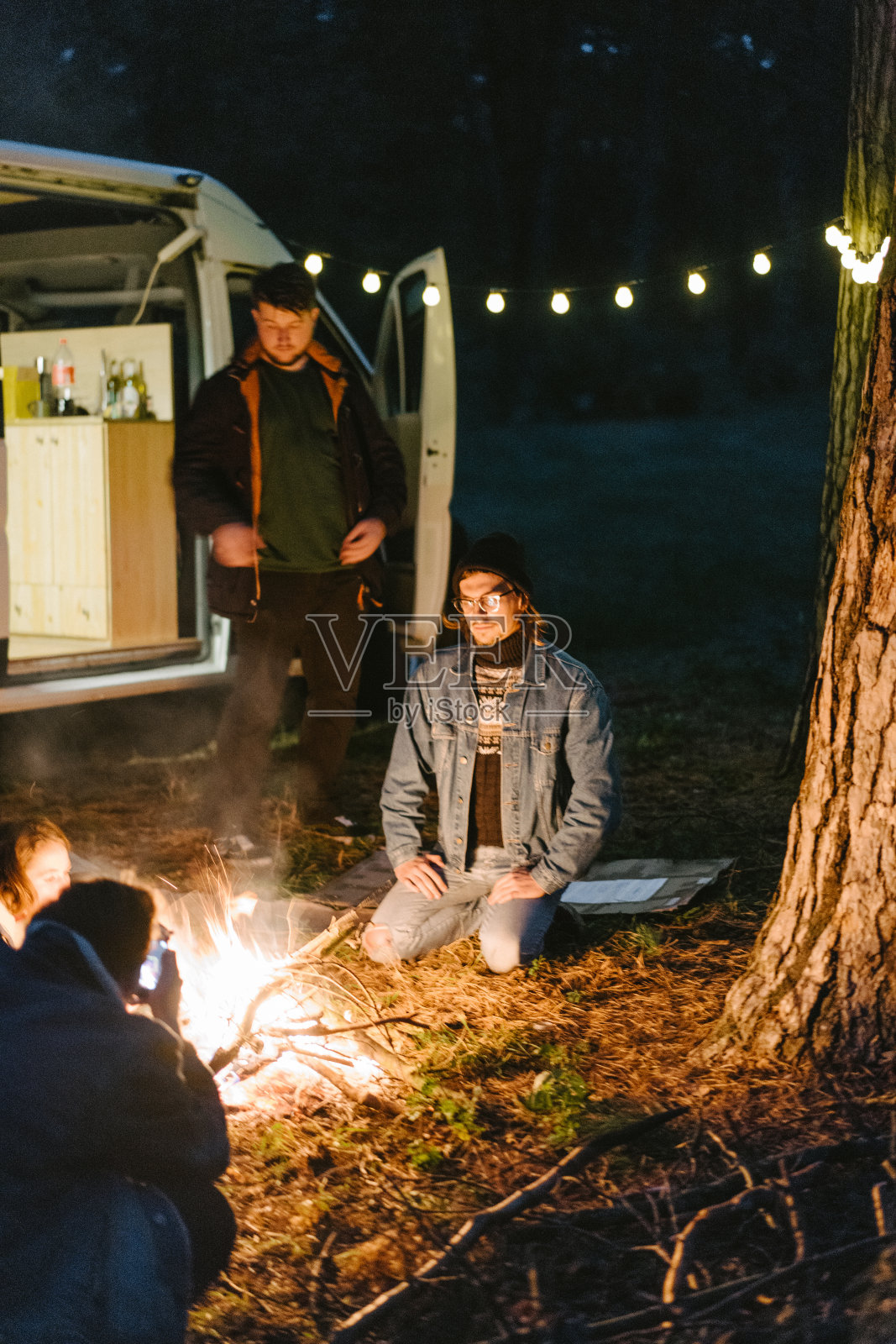 朋友们坐在森林里靠近露营车的篝火旁照片摄影图片