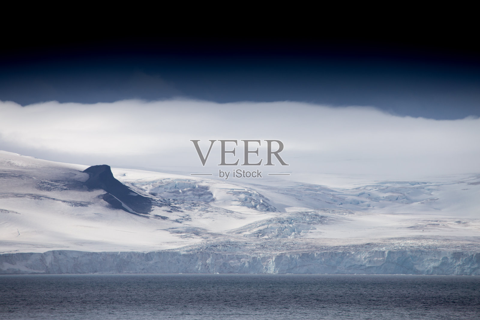 在南极洲，风和云扫过这座山。照片摄影图片