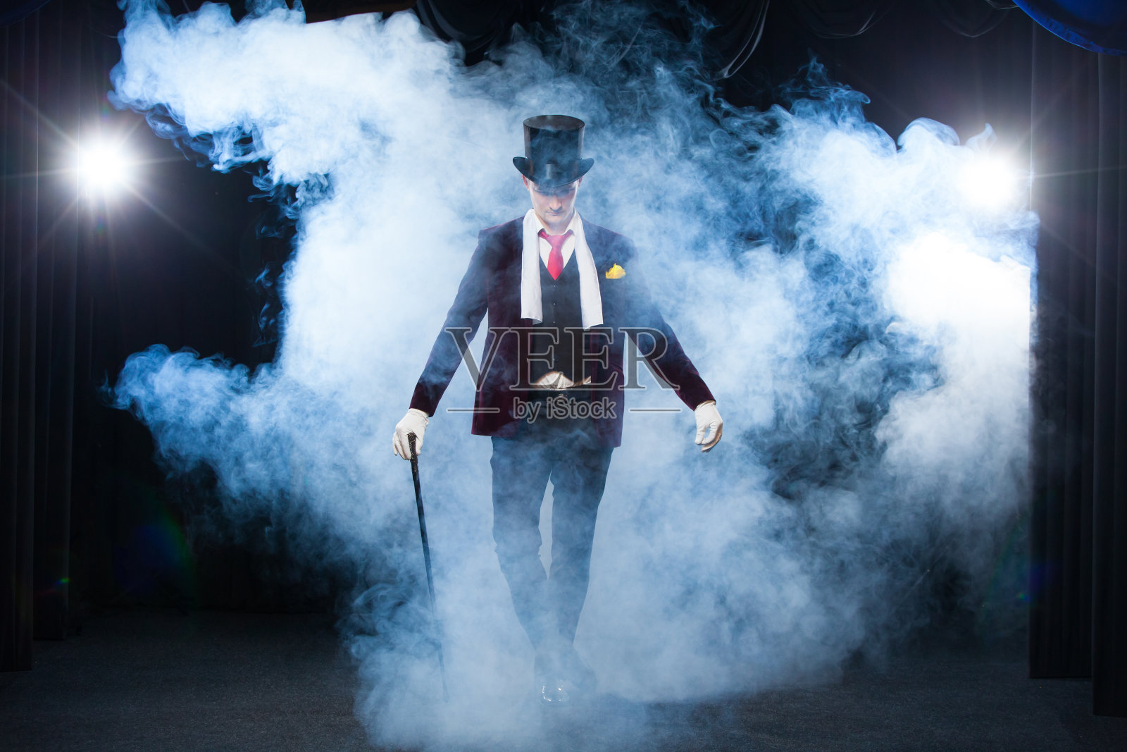 魔术师，变戏法的人，有趣的人，黑魔法，幻觉站在舞台上一根美丽的光手杖。笼罩在美丽神秘的烟雾中照片摄影图片