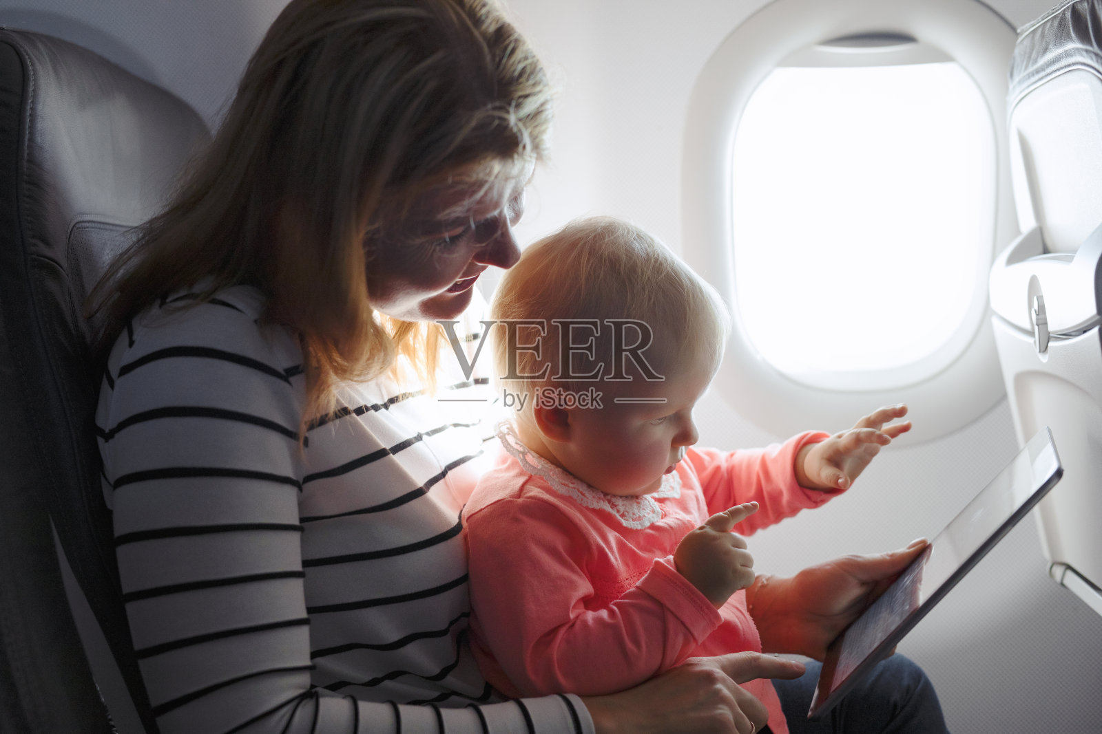 妈妈和孩子在飞机上玩平板电脑。照片摄影图片