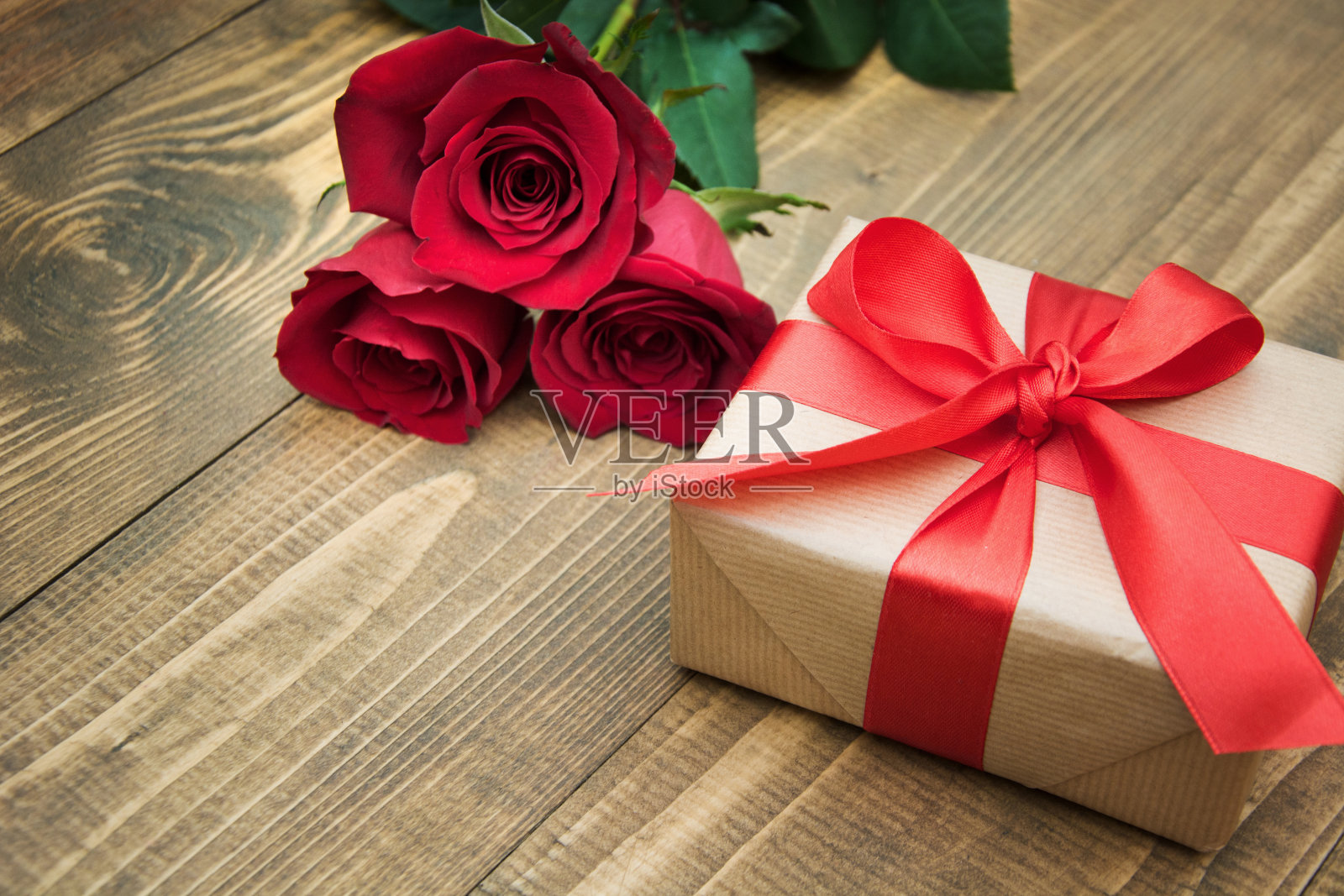 在你的生日或情人节，用一条红丝带和一束玫瑰作为礼物送给一个木制背景上的女人。副本的空间。照片摄影图片
