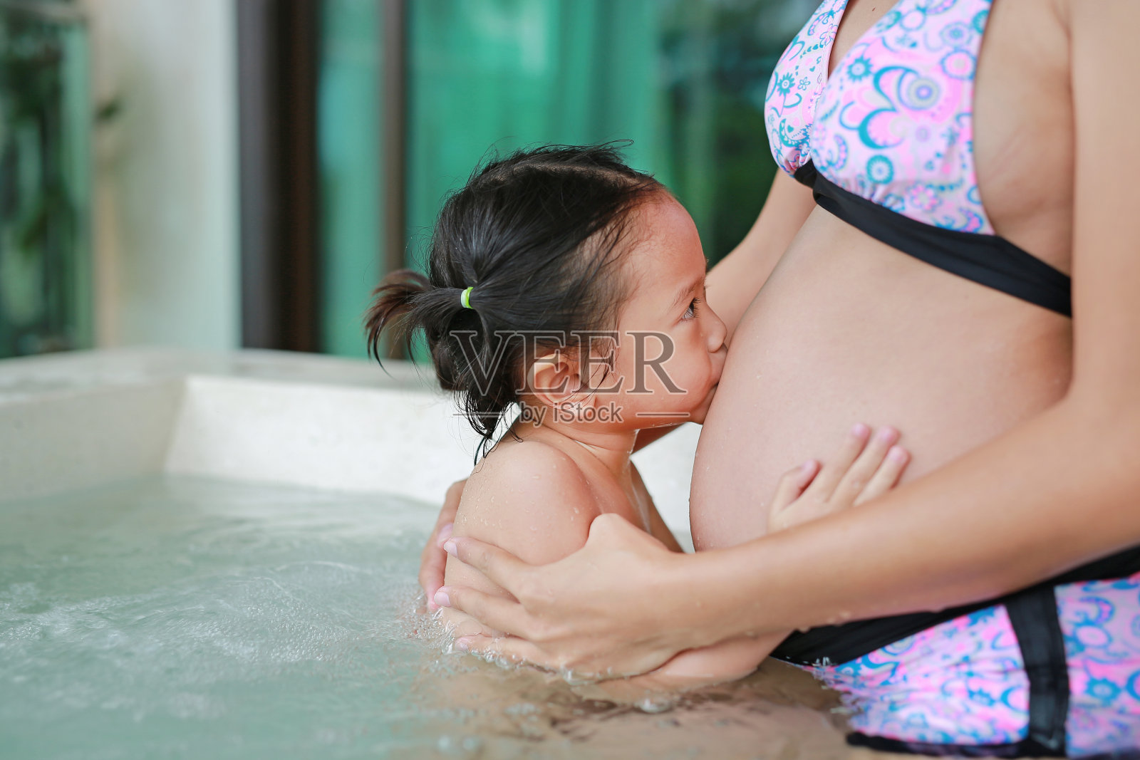 小女孩在浴缸里亲吻孕妇的肚子。照片摄影图片