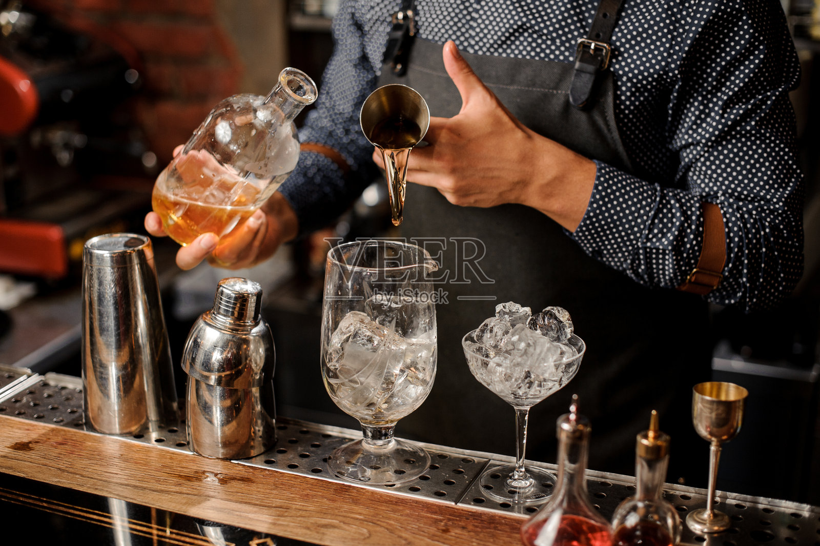 酒保将威士忌和糖浆加冰倒入鸡尾酒杯中照片摄影图片