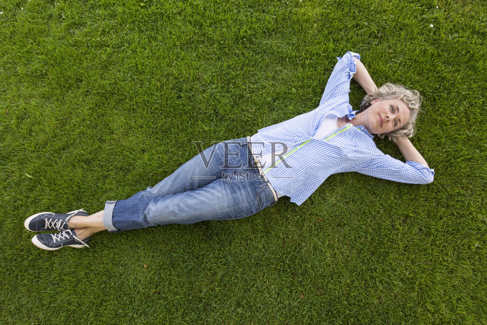 中年妇女，穿着周末便装，在院子或公园的草坪上放松。她脸上带着快乐、满足的表情，看起来就像在做白日梦。照片摄影图片