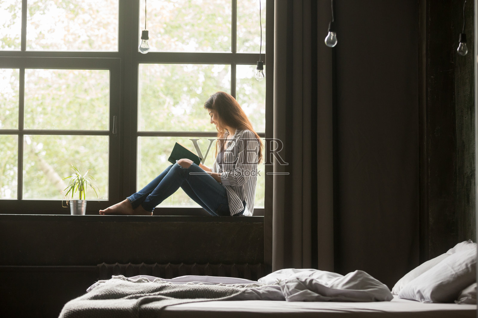 微笑的女人坐在窗台上欣赏一本新的畅销书照片摄影图片