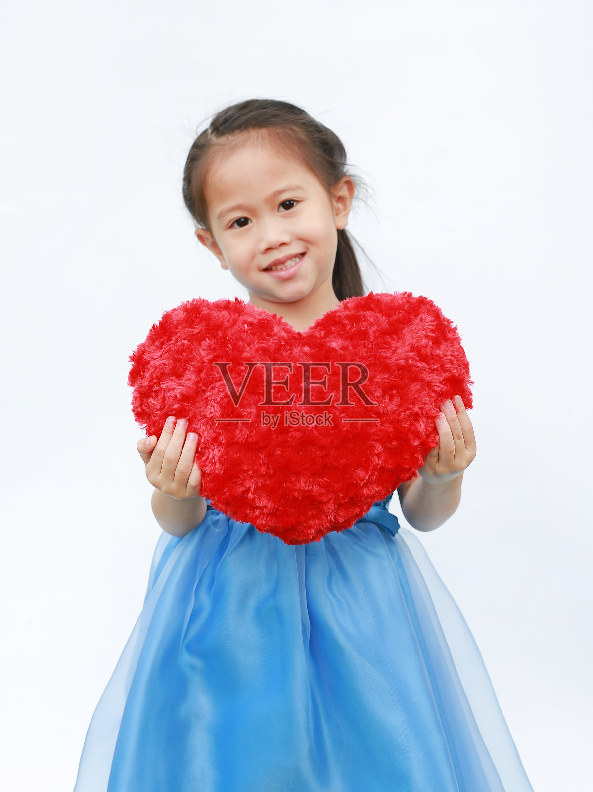 可爱的亚洲小女孩抱着红色的心枕头在白色的背景。照片摄影图片
