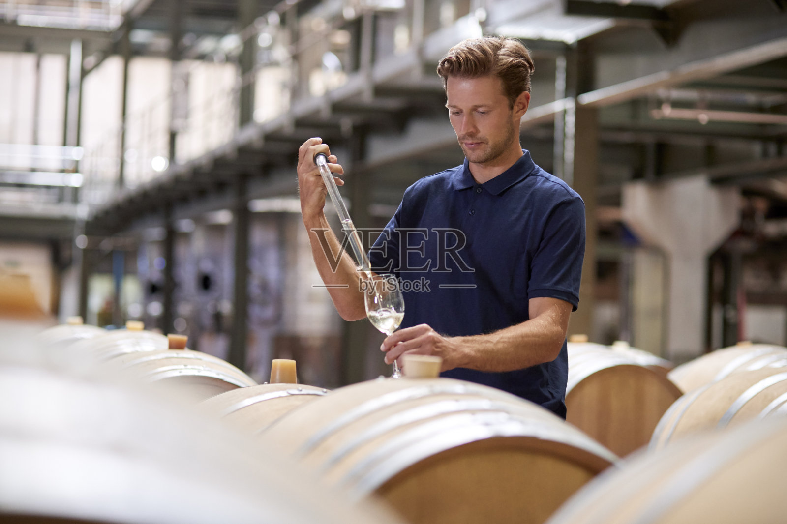 一个年轻人在葡萄酒工厂的仓库里测试葡萄酒照片摄影图片