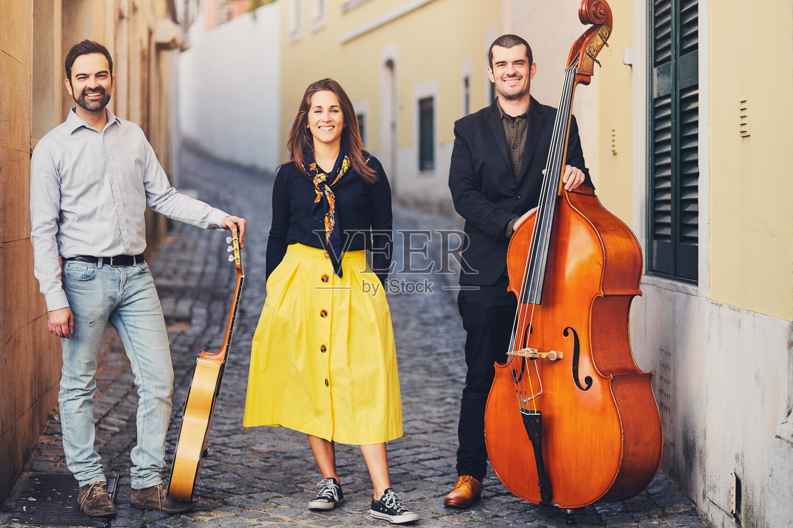 在一条古老的欧洲街道上，三个人组成的音乐团体。乐队由两个男人和一个女孩组成。男人用低音提琴和吉他。非传统的有创造力的人与乐器。照片摄影图片