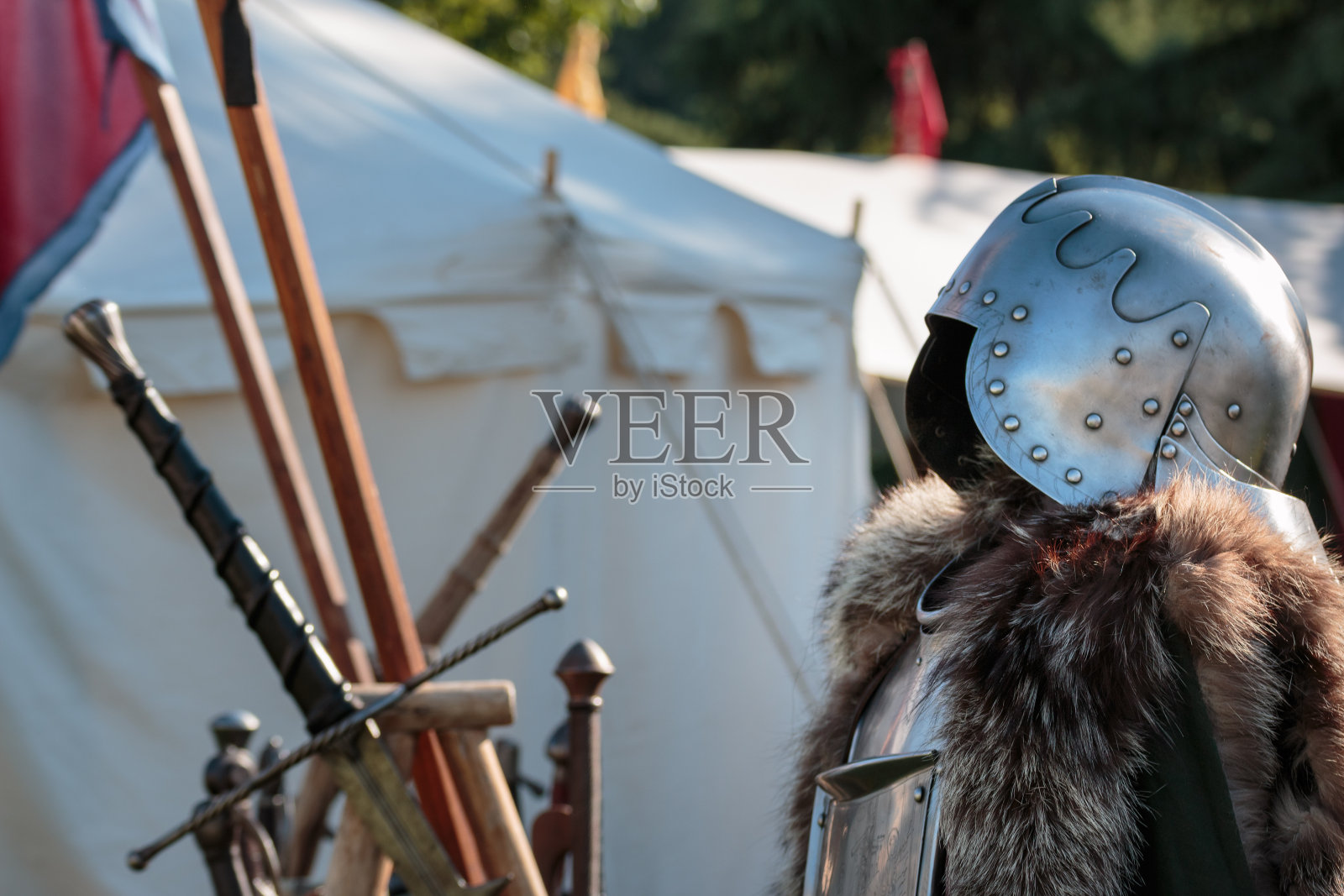 中世纪铁头盔，金属盔甲和毛皮大衣，剑和白色帐篷的背景照片摄影图片