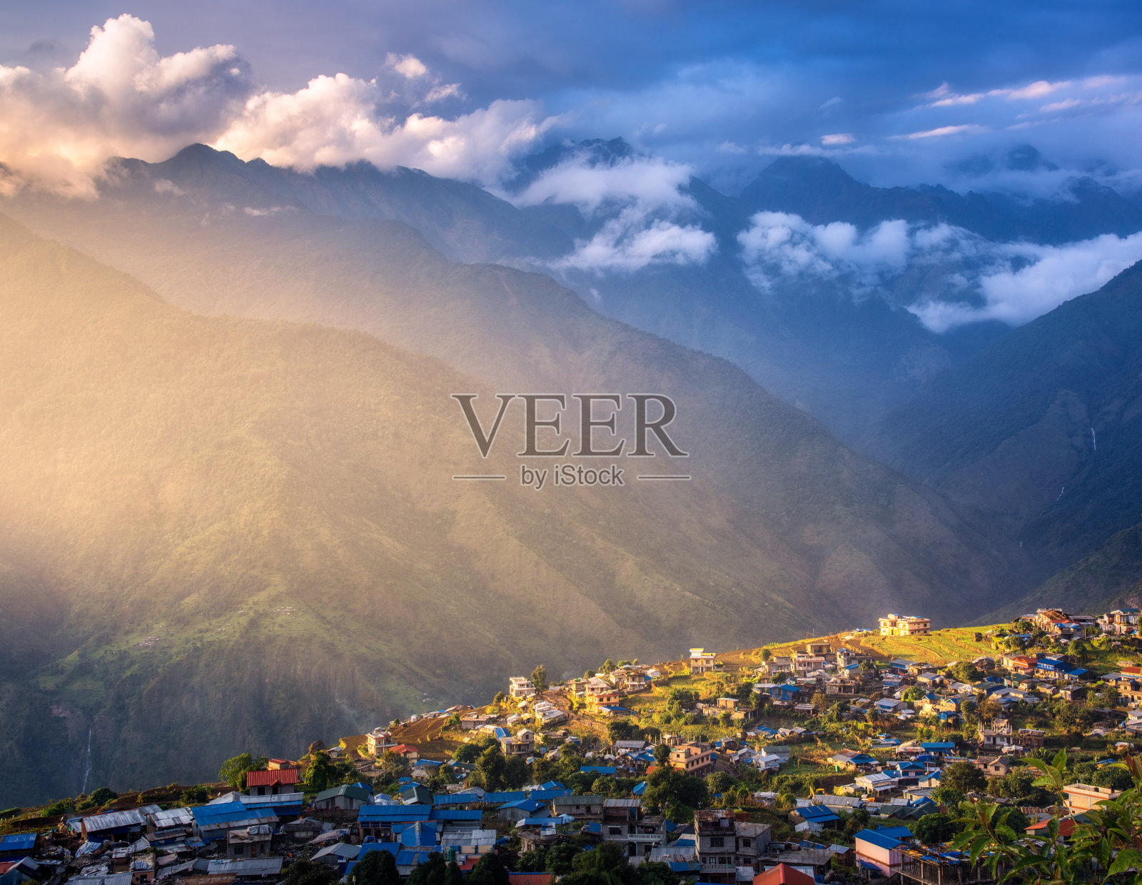 令人惊叹的村庄在山上被阳光照射在日落尼泊尔。风景有房子，蓝天有云，黄色的阳光和高山有绿色的森林。乡村的观点。美丽的喜马拉雅山脉照片摄影图片